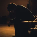 Man sitting on a bench at night holding his head in stress under warm background light, symbolizing How to Stop Overthinking About the Future?