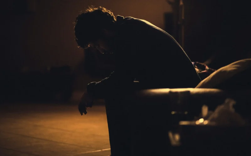 Man sitting on a bench at night holding his head in stress under warm background light, symbolizing How to Stop Overthinking About the Future?